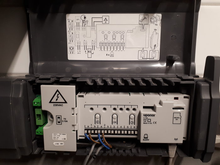 Elcentral för golvvärme med öppet lock som visar kopplingsschema och omkopplade anslutningar.