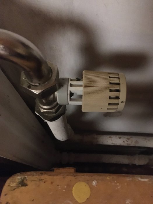 Termostatventil på ett element med numrerad inställningsratt och ansluten kopparrör.