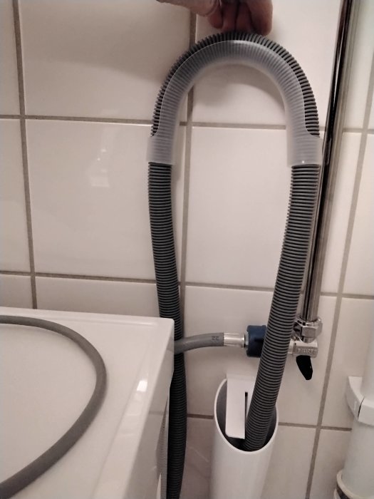 Flexibel slang böjd högt ovanför toalettstolen mot en vägg med kakel.