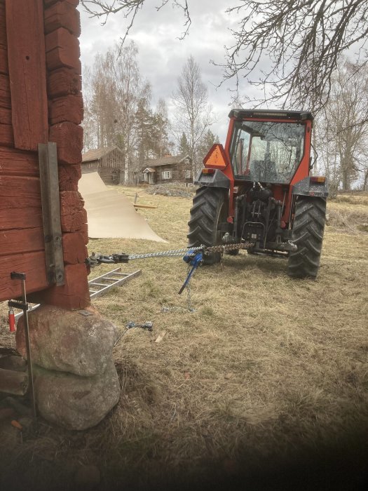 Traktor med vinsch drar en skev lada rak genom att spänna linor runt dess struktur utomhus.