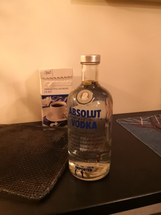 Flaska Absolut Vodka med kryddnejlikor och kardemummakapslar, bredvid en låda bitsocker.