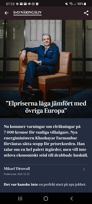 Leende man i kostym sitter på lädersoffa med rubriken om låga elpriser jämfört med övriga Europa.