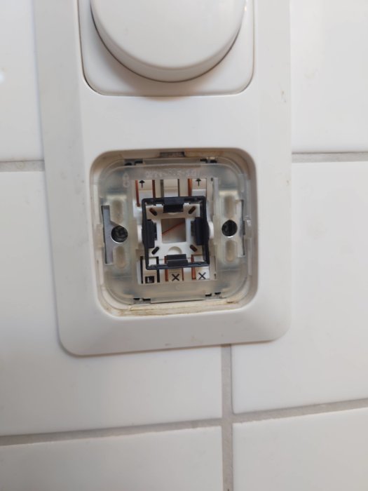 Strömbrytare utan plastknapp monterad på en vägg täckt av vita kakelplattor.