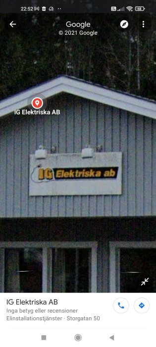 Skylt med texten "IG Elektriska AB" på en byggnads vägg omgiven av träd i skymningen.