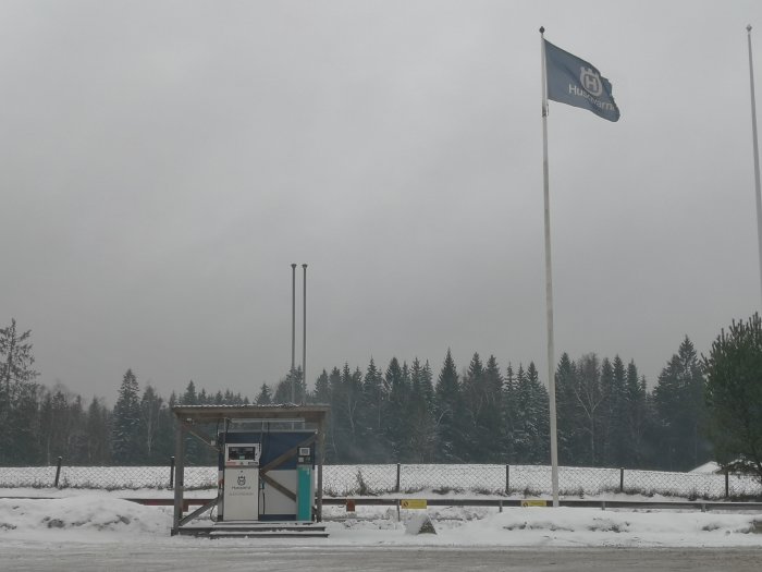 Alkylatbensinmack med Husqvarna-flagga i en snöig skogsbygd.