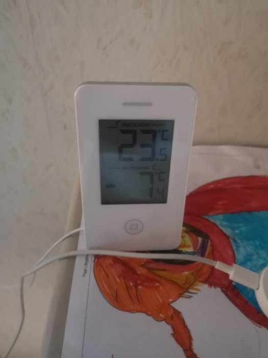 En digitalklocka som visar inomhustemperaturen 23,5°C och utomhustemperaturen 1,4°C, laddas via USB-kabel.