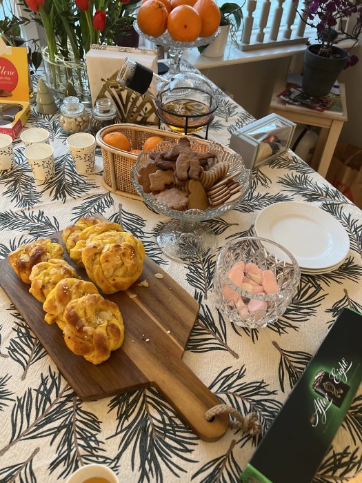 Väl dukat bord med saffransbullar på skärbräda, pepparkakor, kex, lussebullar, och diverse dekorationer.