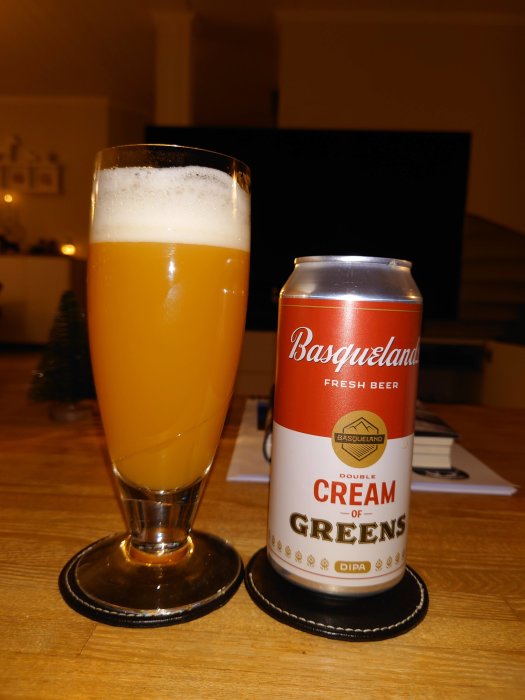 Ett glas med grumlig, orangefärgad DIPA öl bredvid en Basqueland Cream of Greens burk.