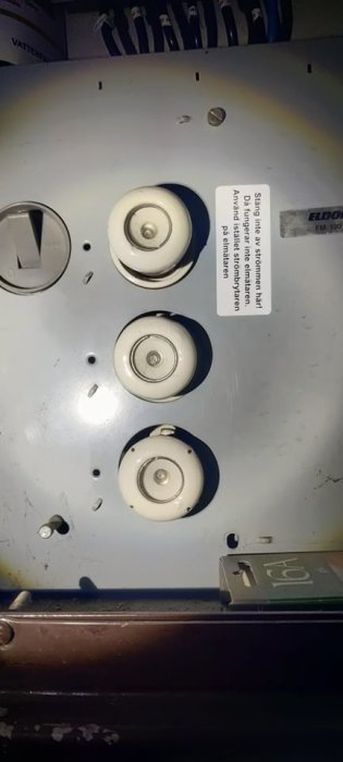 Eldistributionsskåp med tre keramiska huvudsäkringar och en varningsdekal.