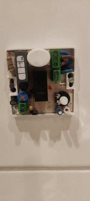 Öppen termostat utan säkring med synliga elektroniska komponenter och ledningar på en vägg.