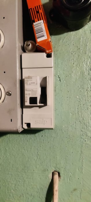Siemens jordfelsbrytare i elskåp med utlöst handtag, mot grön vägg.