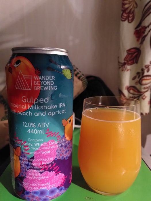 Burk av Wander Beyond Gulped Imperial Milkshake IPA bredvid ett glas med orange öl.