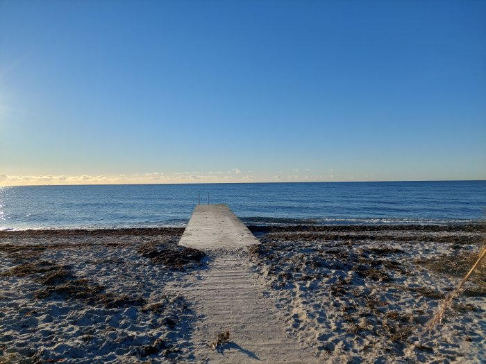 Brygga som leder ut till havet med synliga vindkraftverk i fjärran på en solig juldag.