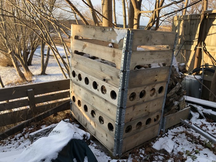 Trästapel med ventilerade kragar med sticksågade öppningar för bättre ventilation, omgiven av snö.