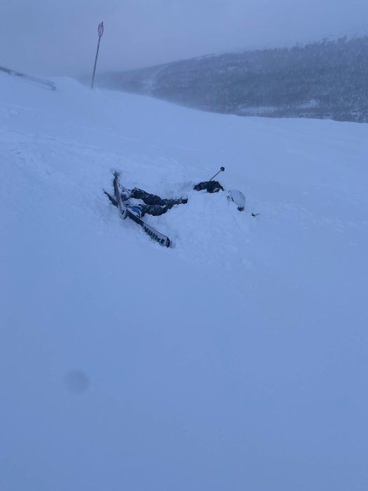 Person som fallit i snön med skidor bredvid sig under en snöig dag.
