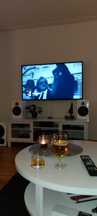 Vardagsrum med TV som visar en video, två glas dryck på bordet och ljudanläggning vid sidan.