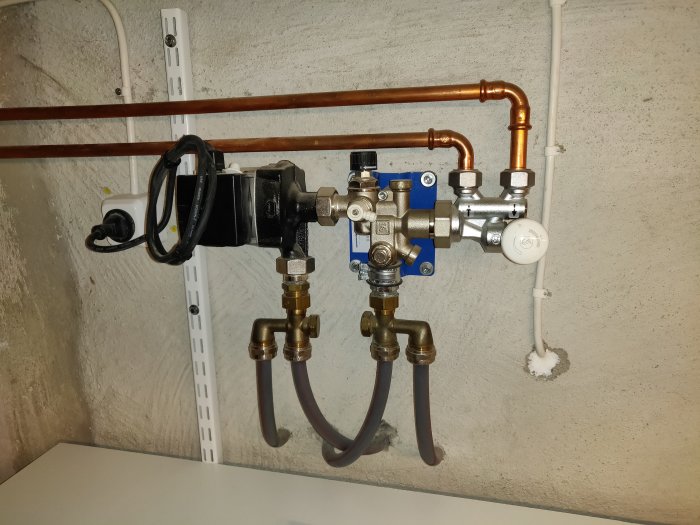 Golvvärmefördelare med termostatventil, ställdon och kopparledningar mot betongvägg.