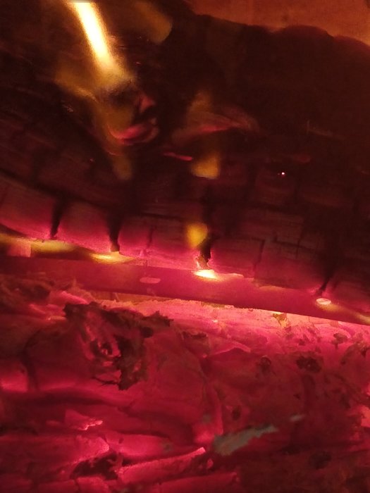 Glowing embers and objects inside a wood-burning stove, likely metal items being heat-treated.