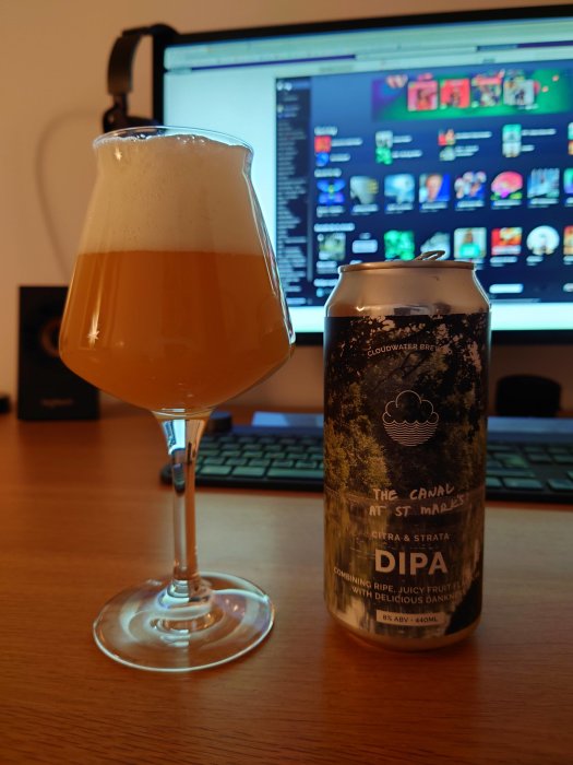 Ett glas öl bredvid en ölburk från Cloudwater med en datorskärm i bakgrunden.