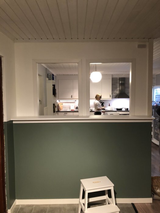 Renoverat kök med grön halvvägg, vit inredning och en person i bakgrunden.