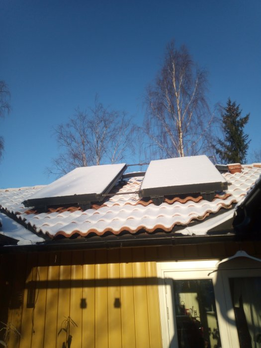 Solpaneler täckta med snö på ett hustak med 27 graders lutning mot klarblå himmel.