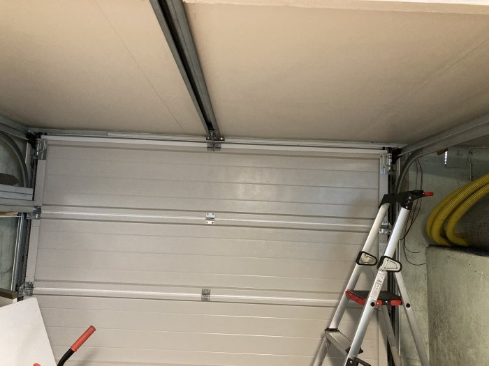 Installerade spottar ovanför en stängd garageport samt en stege och verktyg.