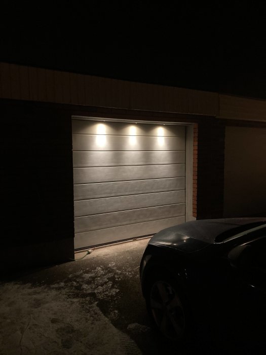 Nyinstallerade spotlights med 2700k belysning över en garageport på kvällen, bil delvis synlig.