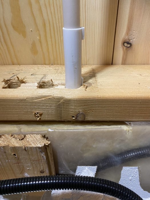 En närbild av en klumpig elinstallation med synliga PVC-rör och trasiga träplank, tecken på amatörmässigt arbete.