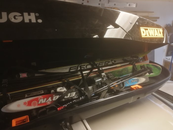 En öppen skidbox på en bil med skidor, snowboard och teleskopstänger.