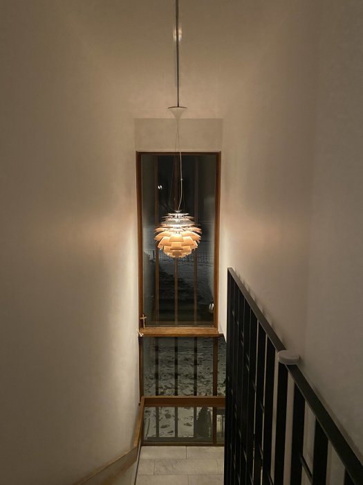 Modern taklampa i trapphus med beige väggar och trädetaljer.