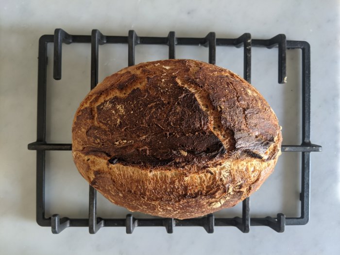 Nybakat bröd med krispig skorpa på ett kylställ, bakat i upphittad återvunnen gjutjärnskastrull.
