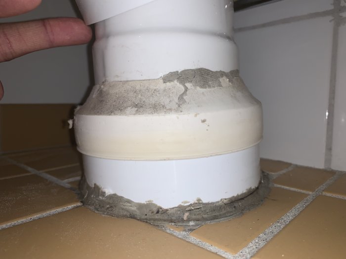 Hand visar en spricka i toalettstolens gummimuff och tätning nära golvet.