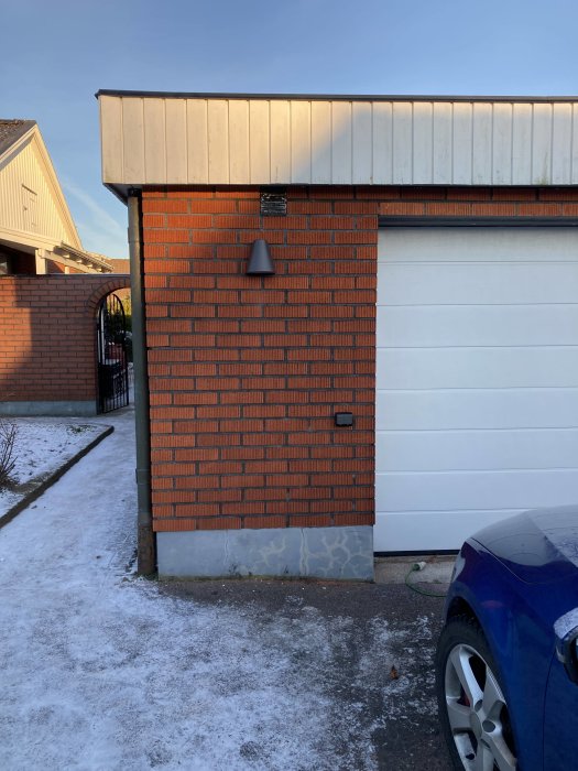 Nyinstallerad lampa och uttag på tegelvägg vid garage, med snöig omgivning.