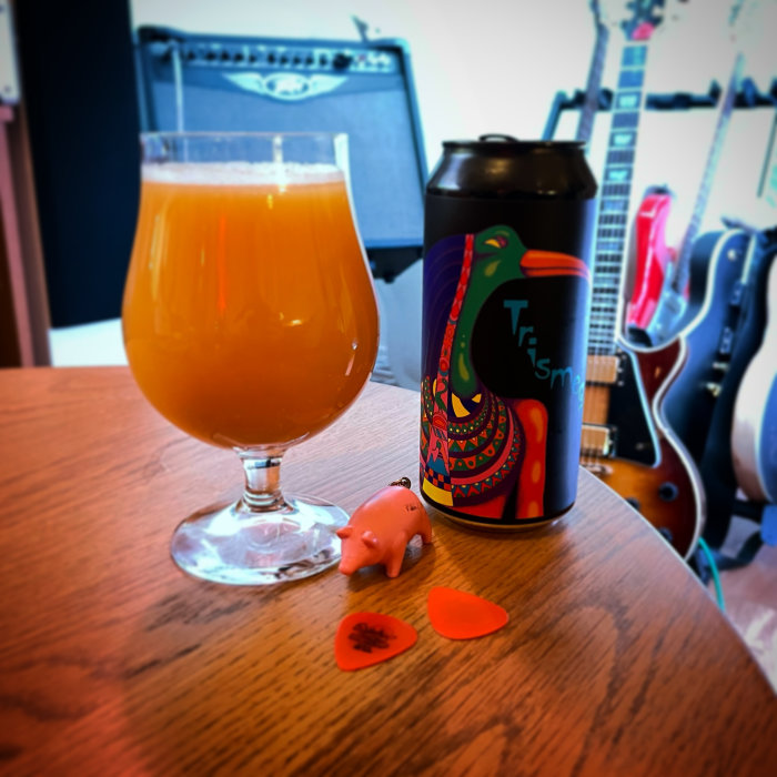 Ett glas med orange dryck, konstnärligt ölburk, småprylar och gitarrer i bakgrunden.