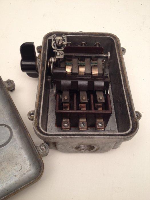 Äldre eluttag med öppnat lock och synliga kopparanslutningar på vit bakgrund.