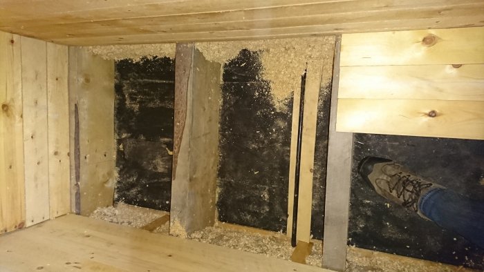 Attic renovation with visible black metal conduit for electrical wiring, wood framing, insulation, and a person's foot for perspective.