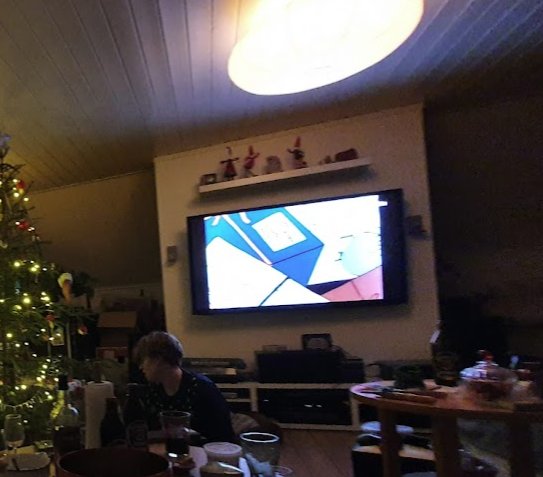 Vardagsrum med TV monterad på vägg, dolda kablar, snedtak och juldekorationer.