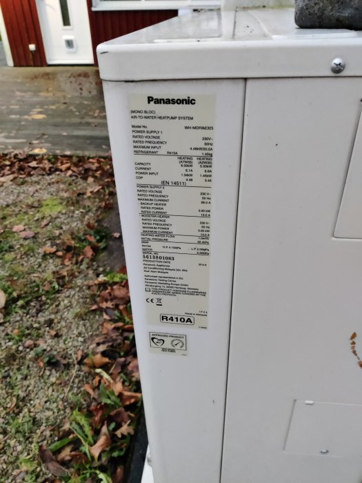 Etikett med teknisk information på en Panasonic luft-till-vatten värmepump, utomhus.
