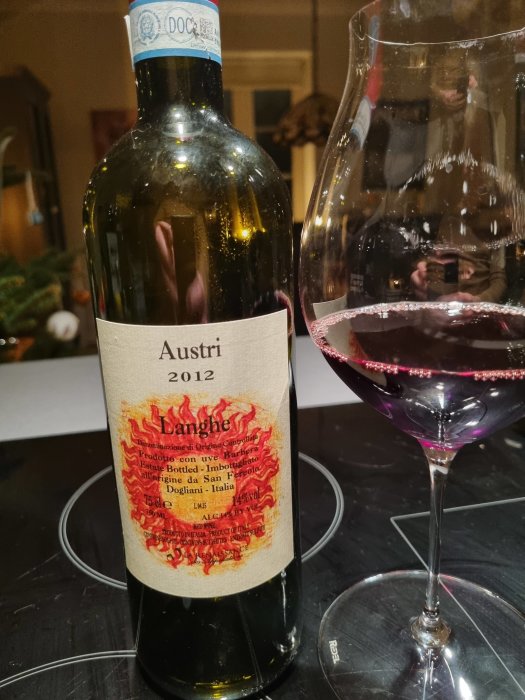 Flaska av Austri Langhe 2012 vin vid sidan av ett nytt pinot noir-glas delvis fyllt med rött vin.
