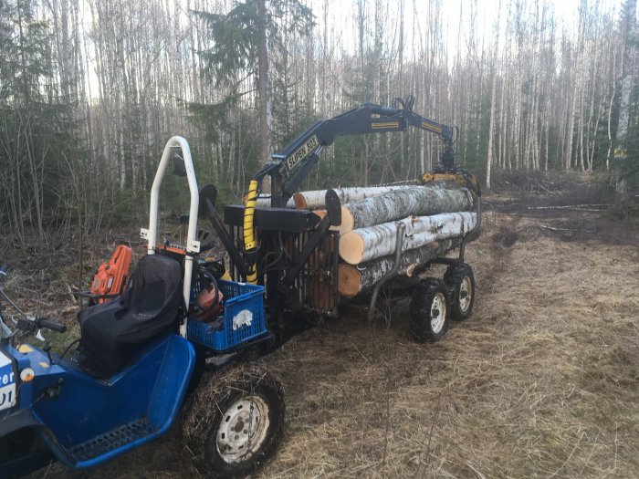 Skogsmaskin med kran som lastar sågtimmer på en vagn i skogsmiljö.