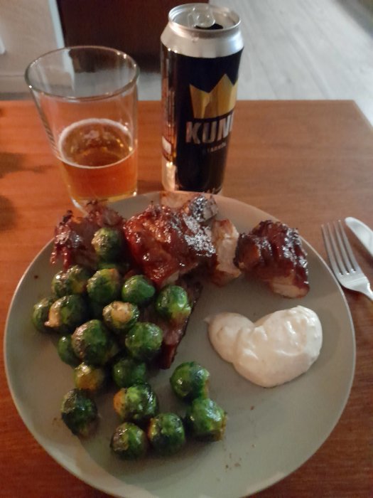 Grillade revben med brysselkål och klick aioli på en tallrik bredvid ett glas öl och en ölburk.