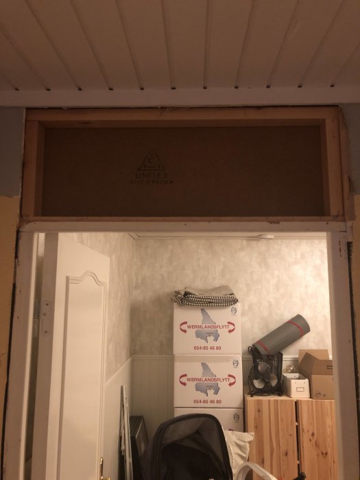 Renoverad hall med öppet utrymme ovanför dörr där masonitskiva används som täckning.