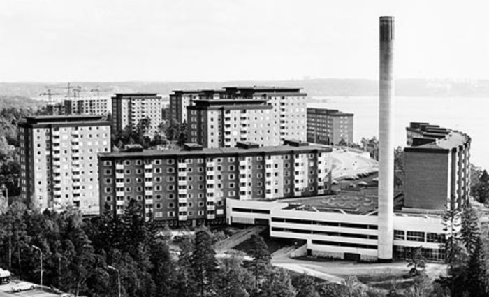 Svartvit bild av en fjärrvärmecentral med hög skorsten intill flerbostadshus från 1970-talet.