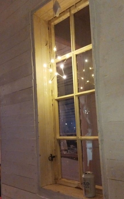 Ett gammalt fönster från 1850-talet inbyggt i ett trapphus, omgivet av en trävägg och dekorerat med ljusslinga.