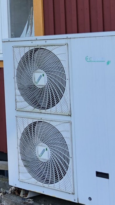 Utedel av en värmepump märkt "Ecozon" mot en röd husvägg.