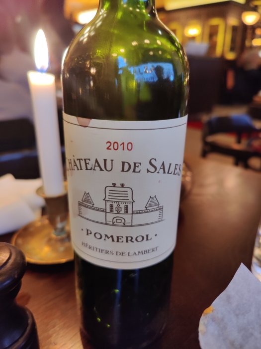 Flaska Pomerol vin, Chateau de Sales 2010, på ett bord med levande ljus i bakgrunden.