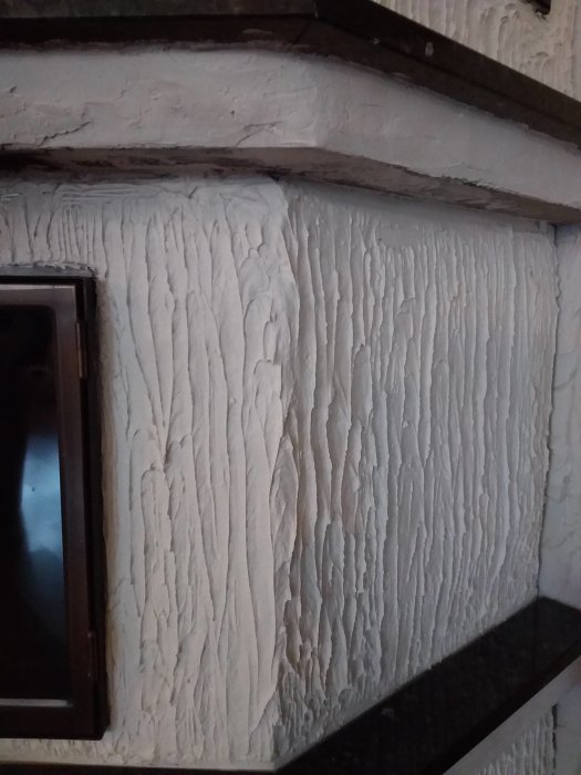 En vägg med grov, räfflad cementputs liknande en pizzeriavägg och en del av en svart kamin.