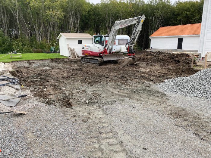 Utgrävning för dubbelgarages grund med grävmaskin, grusbeläggning och tomthål.