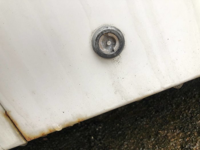 Närbild av ett lås på en vit värmepump som verkar kräva en specialnyckel.