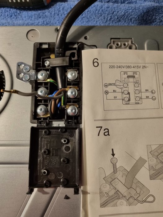 Anslutningspunkt för induktionshäll med urkopplad grå kabel och instruktionsbok.